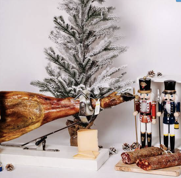 Jambon ibérique entier sur jamonero devant un sapin de Noël enneigé avec soldats de bois