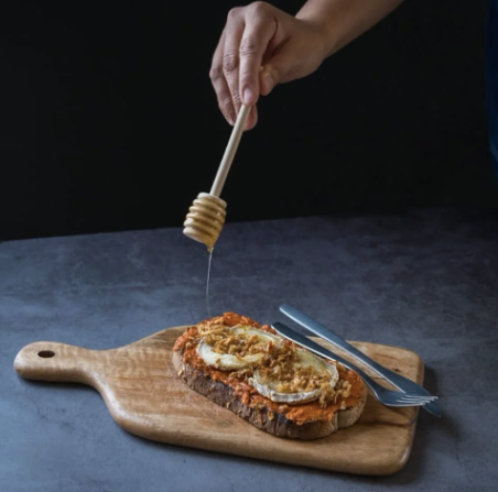 Tartine de sobrasada ibérique avec fromage et filet de miel versé sur planche en bois