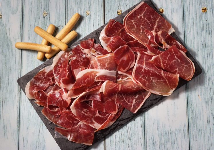 Planche ardoise de jambon ibérique tranché avec gressins sur table en bois clair