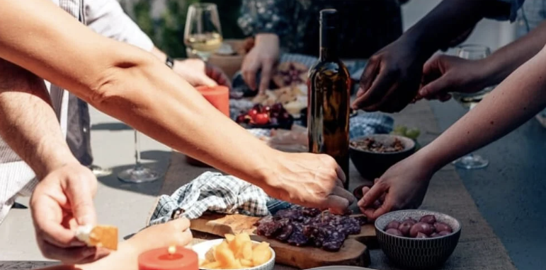 Groupe d'amis partageant un apéritif en extérieur avec charcuterie, fromage et vin blanc
